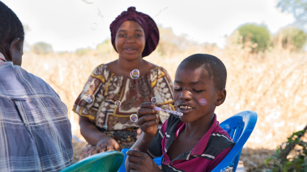 Joseph sits outside with his family, blowing bubbles