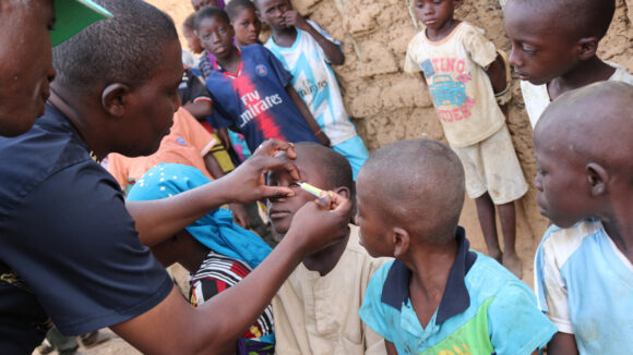A doctor carries out an eye screening surrounded by a community of people.