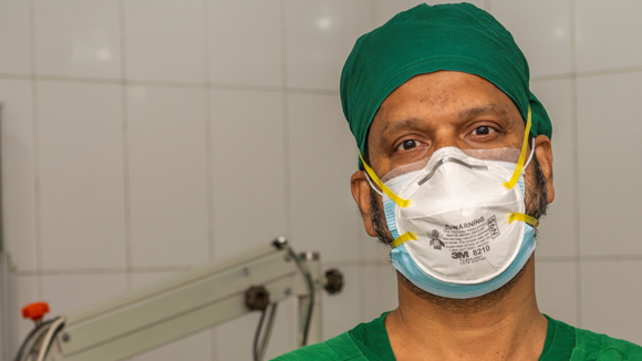 An eye surgeon wearing a medical face mask and scrubs.