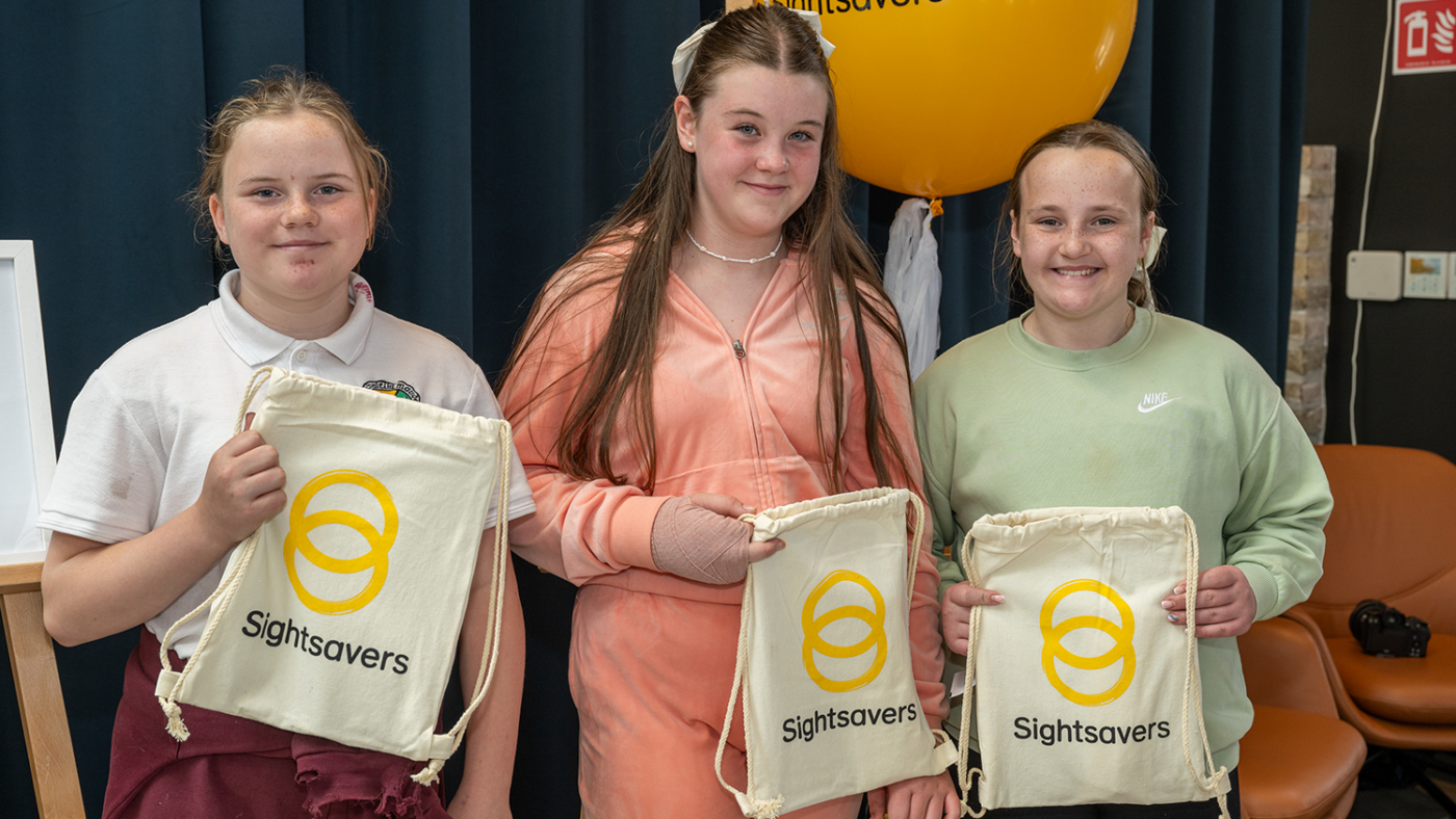 Three girls hold up their Sightsavers branded bags.