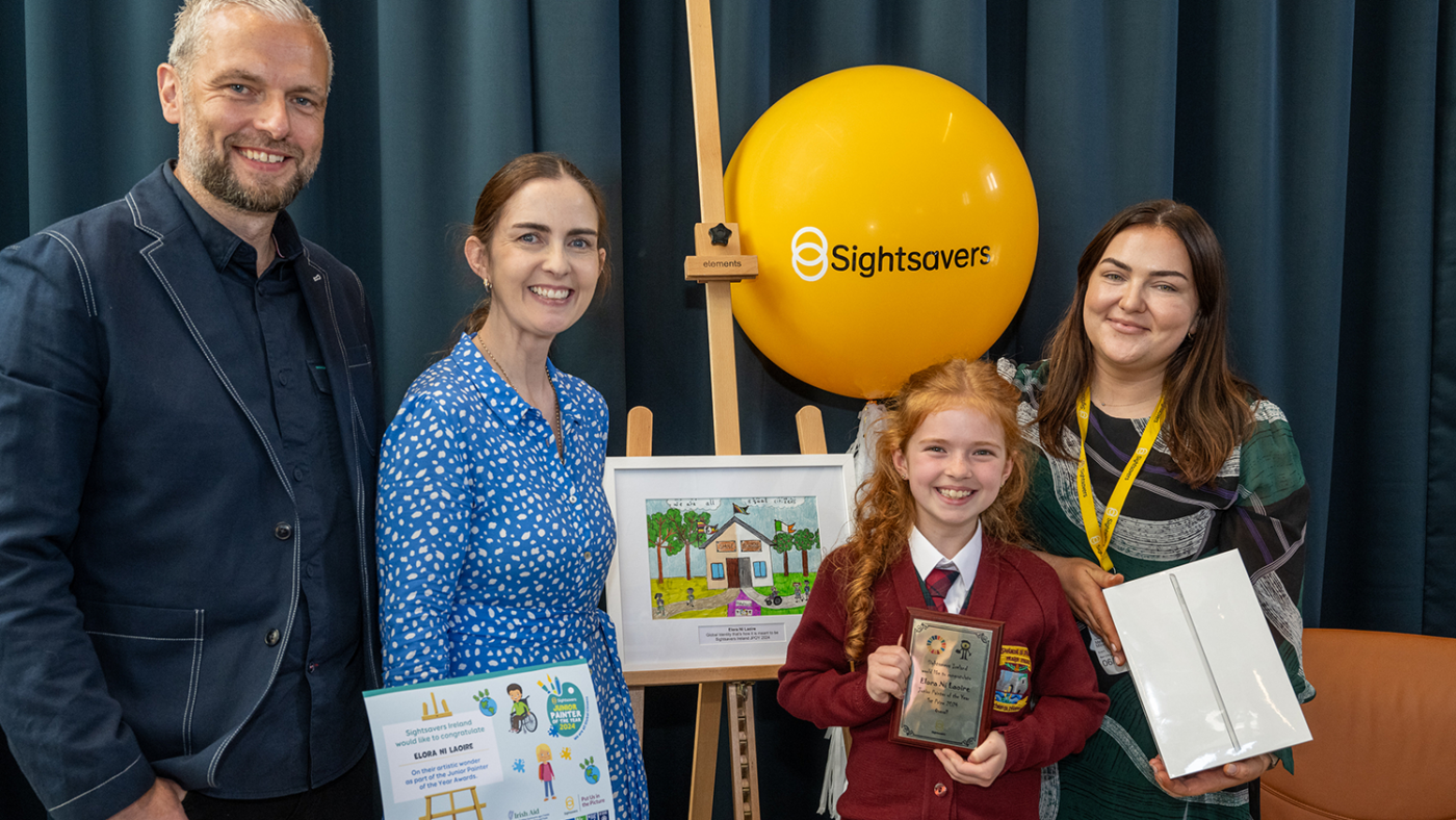 Elora smiles as she stands next to her painting holding her trophy.