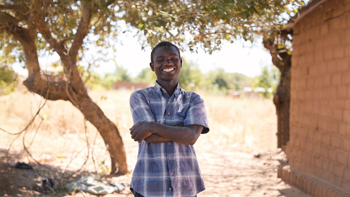 Ezekiel stands outside with his arms crossed and smiles widely at the camera.