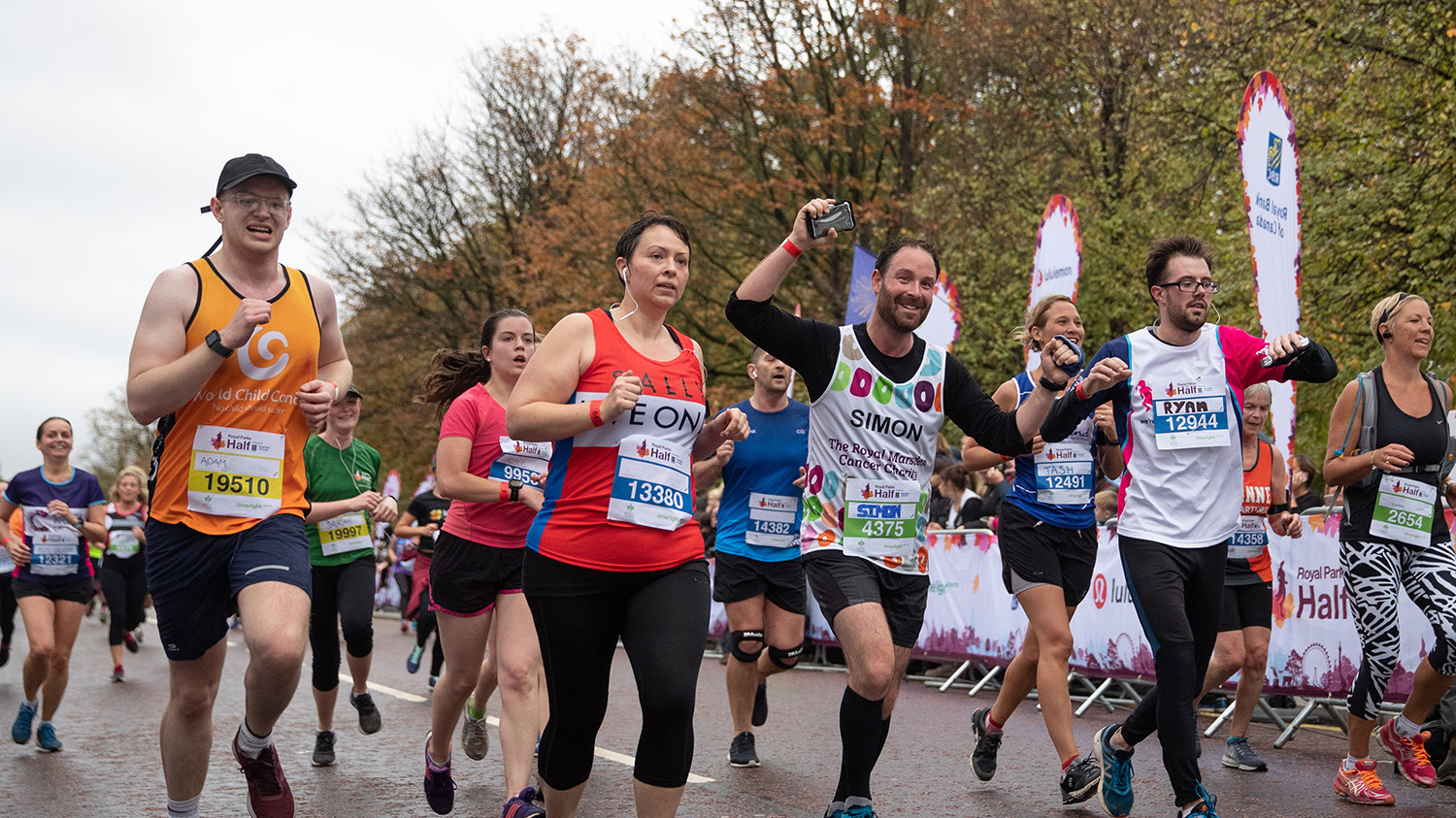 A group of runners race along a road near a park.
