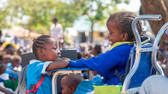 Two young girls talk to each other in a playground. One of the girls has a physical disability and is using a wheelchair.