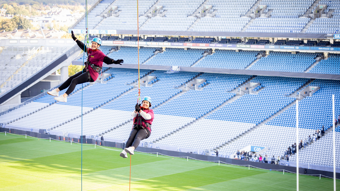 Two women in harnesses dangle from the roof of a stadium during the abseil.