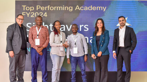 Sightsavers’ programme officer Salome Njeri Mbugua-Mutua receives the award on stage alongside two academy instructors.