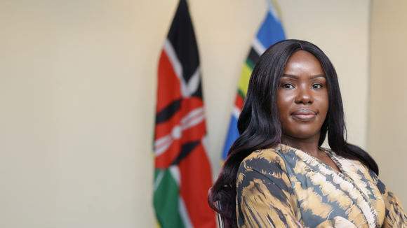 Lydia, an IT Bridge Academy graduate, smiles while standing in front of the Kenyan flag.