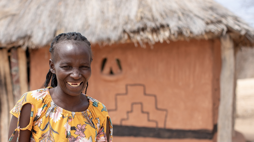 Maria smiles in front of house with a thatched roof.