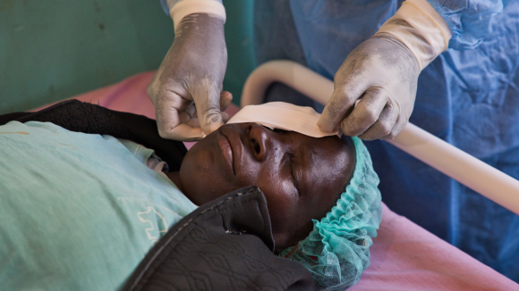 Maria, lying down on a surgery bed with a doctor placing bandages over her eyes.