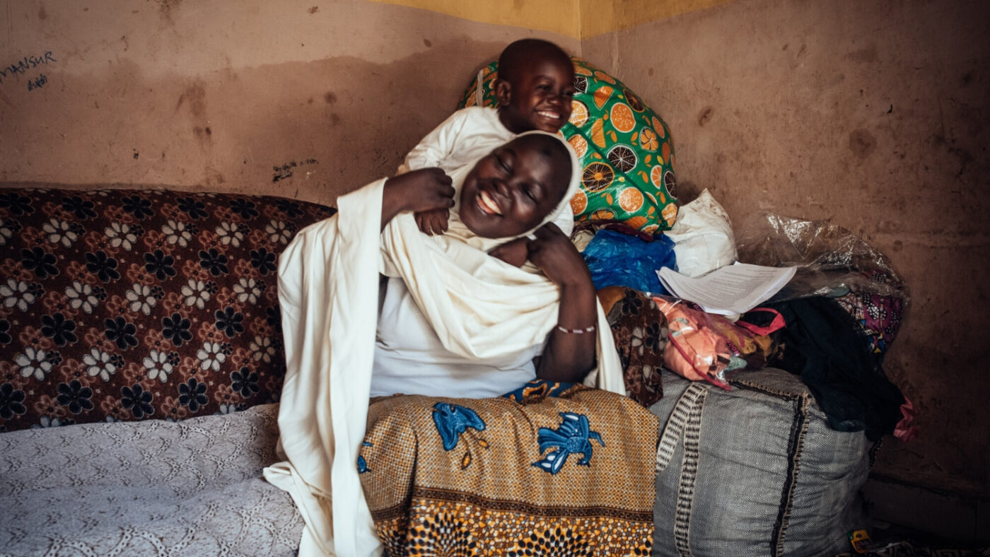Muhammad climbs onto Halima's back to play. They are both laughing.