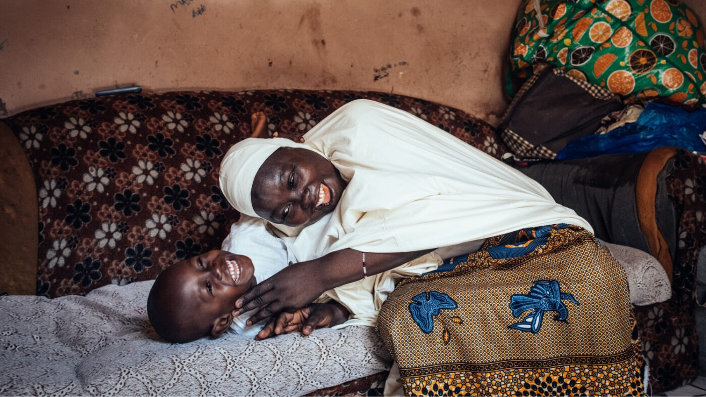 Halima and Muhammad play and laugh together on the sofa.