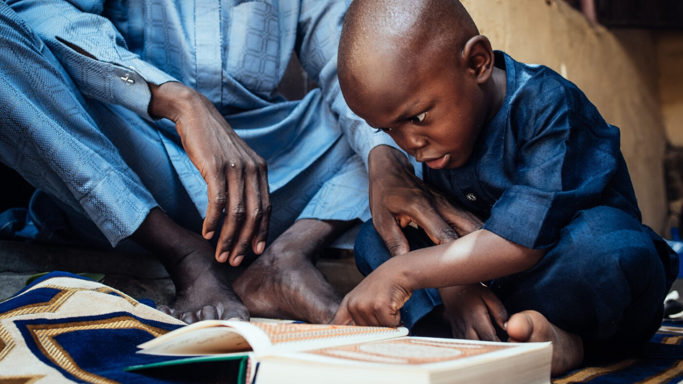 Muhammad tips his head close to a book as he struggles to read due to his cataracts.