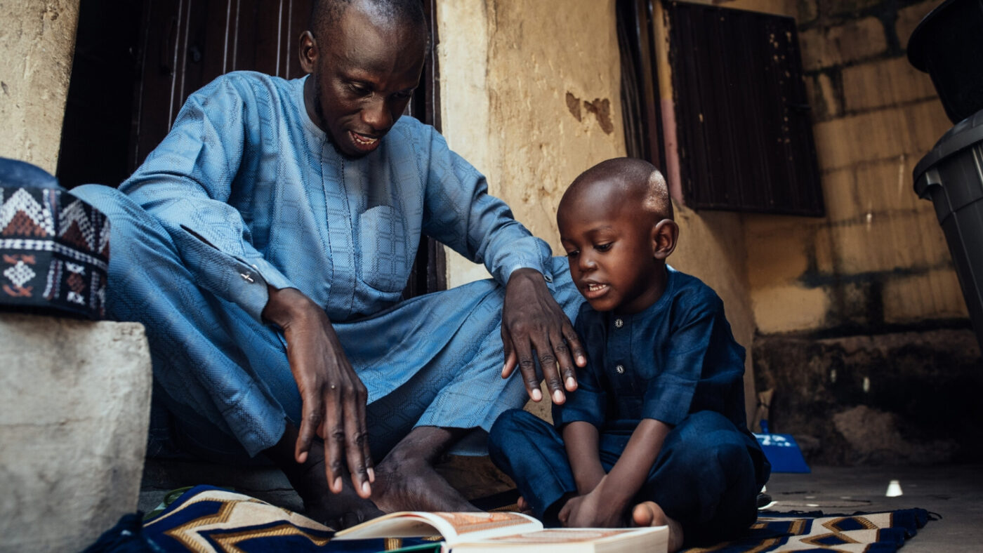 Muhammad sits with his father, Abubakar, looking at a book.