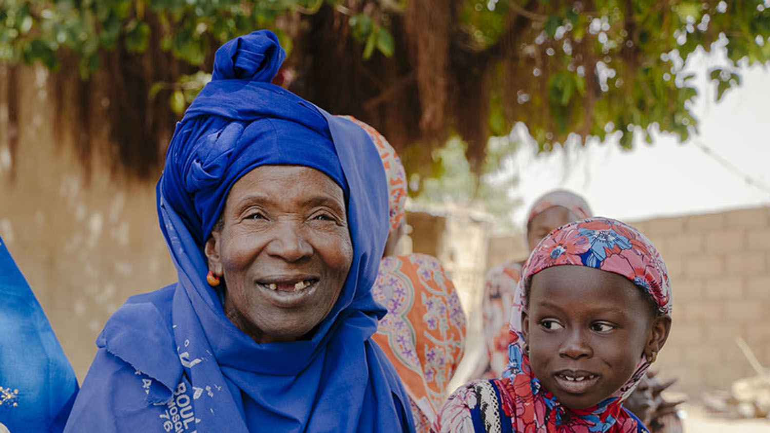 Nar, who had successful treatment for trachoma, sits outside with her two grandchildren. They are all smiling.