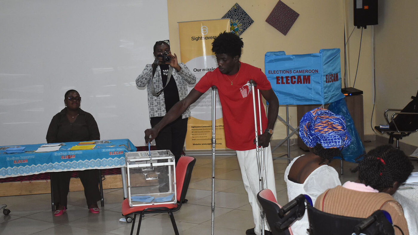 A man using crutches puts his voting ballot into a box.