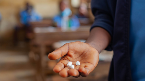 Tablets are shown in the palm of a hand with a blurred out classroom in the background.