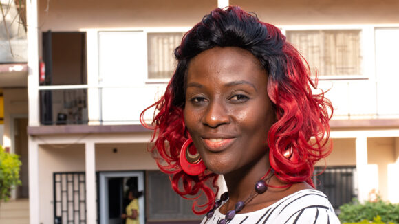 Pascaline, a woman from Cameroon with vibrant red curly hair, smiling in the sunshine.