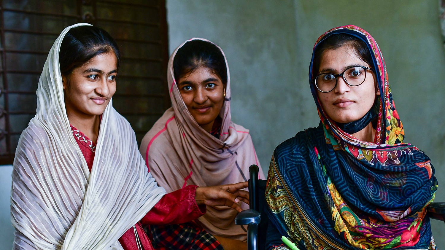 Aasiya sits in her wheelchair alongside her two sisters.