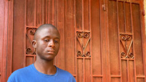 Abubakarr stands in front of an ornate wooden door.