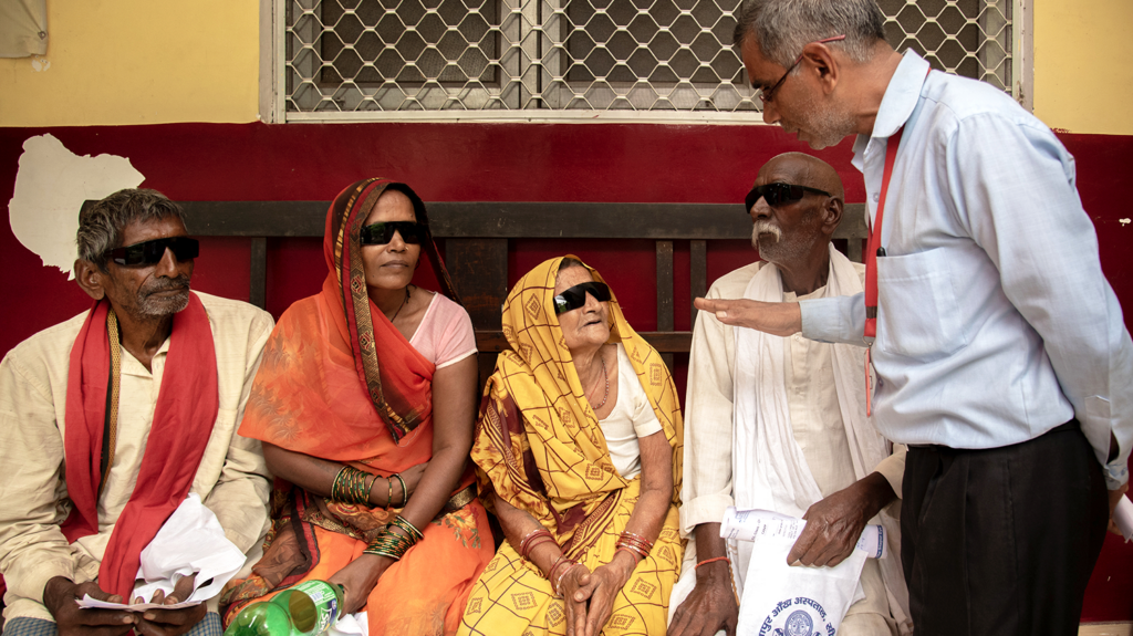 Four patients with protective glasses talk to a man in a suit.