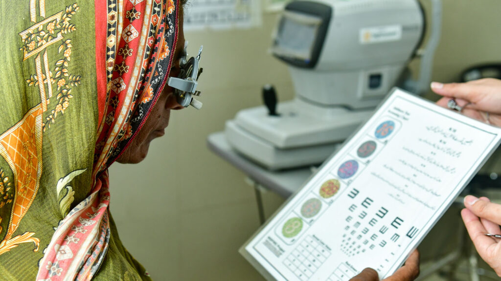 A woman wearing optical glasses reads from a hand-held chart during an eye test.