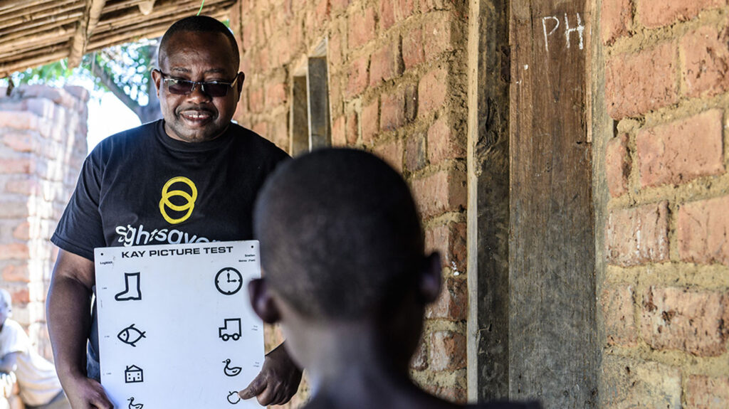 An eye health worker holds a chart with symbols on during a girl's eye test.