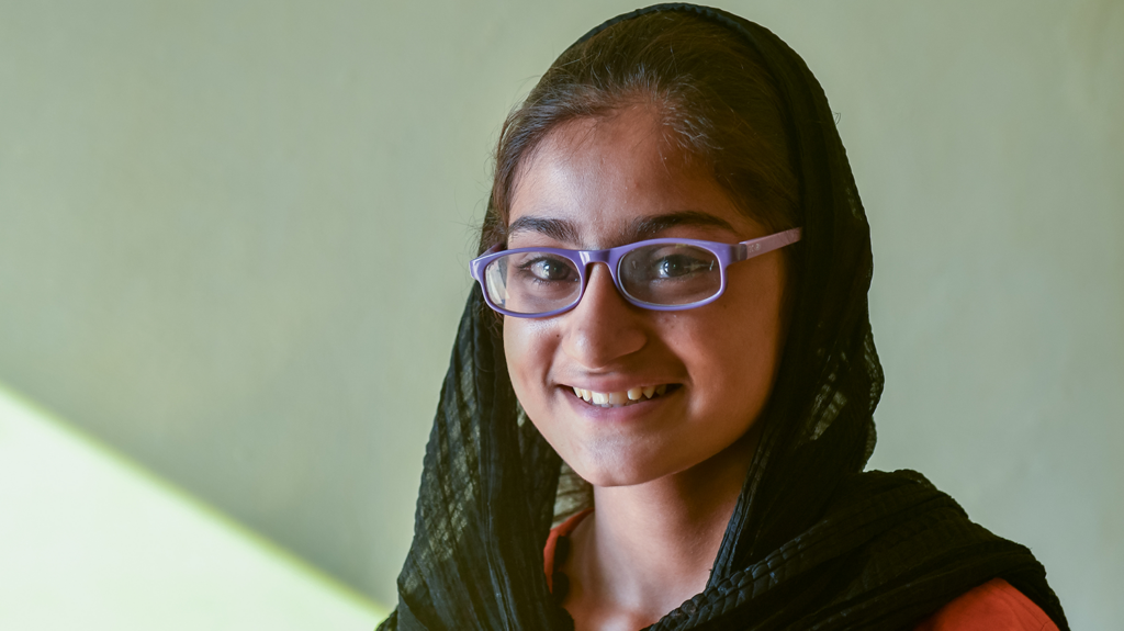 A girl wearing glasses smiles.