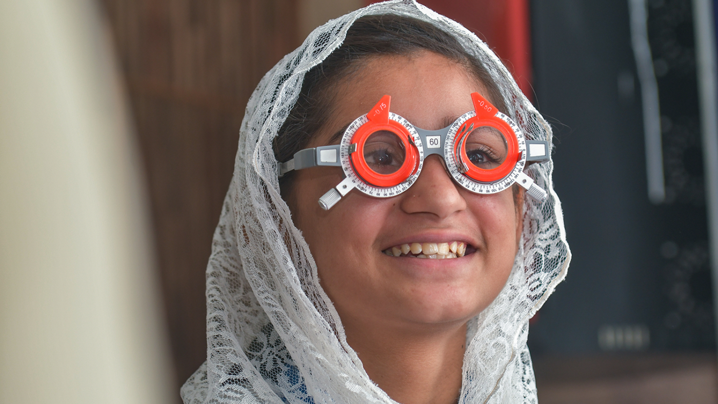 A girl wearing trial frame glasses looks happy during an eye test.