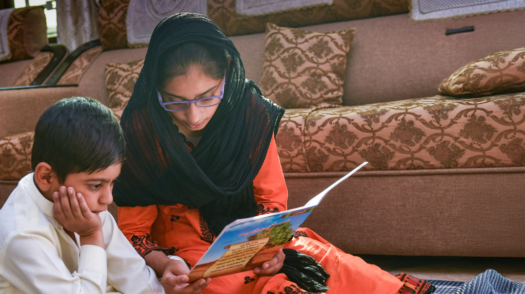 A young girl reads a book to a little boy.