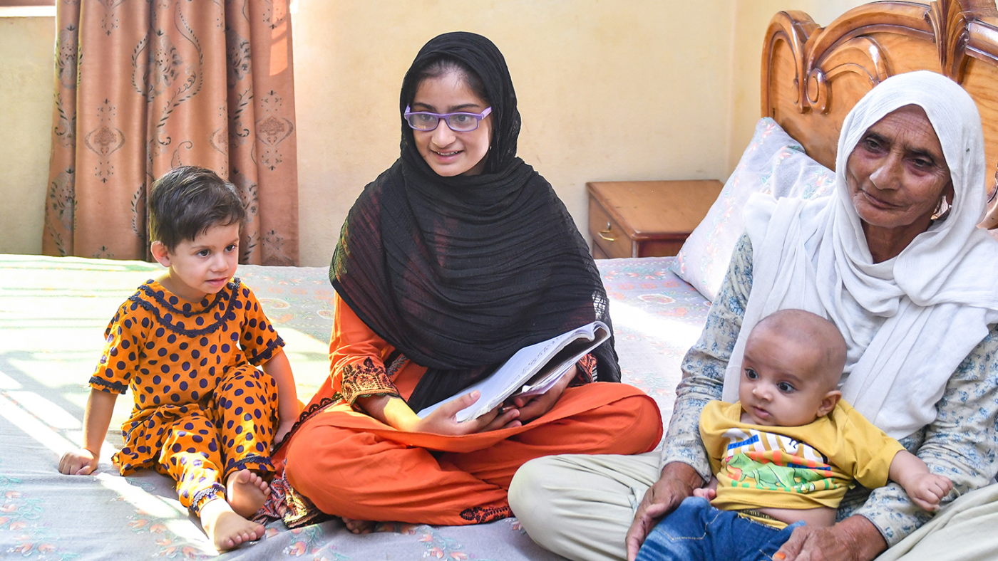 A girl and a toddler sit beside an older woman holding a baby.