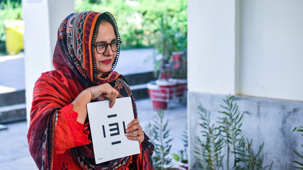 A woman wearing a head scarf holds an eye test chart.
