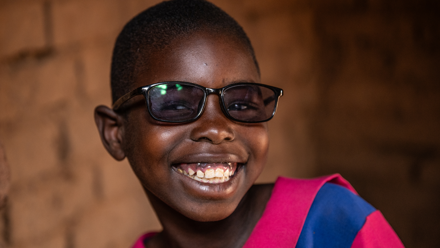Melia in front of a brick wall smiling, wearing her protective dark glasses.