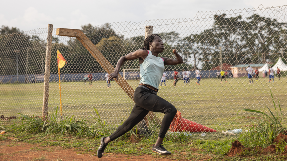A female athlete is midstride while running around an athletics track. Her arms are very toned, and she's missing her left hand.