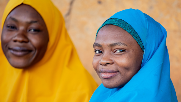 Two women wearing brightly coloured headscarves smile at the camera.
