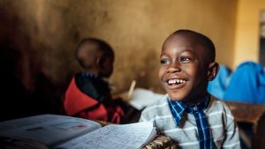 Muhammad, a young boy from Nigeria, smiles while sitting at his desk at school.