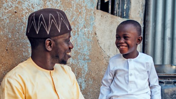 Muhammad, a young boy from Nigeria, smiles at his father Dawud outside their home.