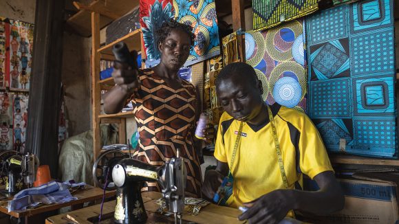 A woman holds some thread while a man works at a sewing machine.