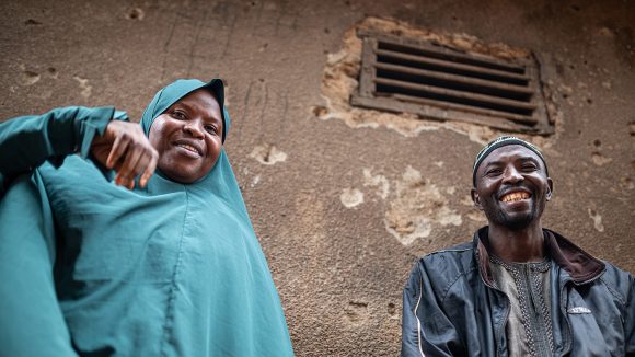 A woman wearing a teal chador sits next to a man. The couple are smiling.