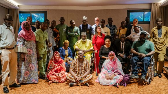 A group of men and women pose for a photo. Some of the people are using wheelchairs or crutches.
