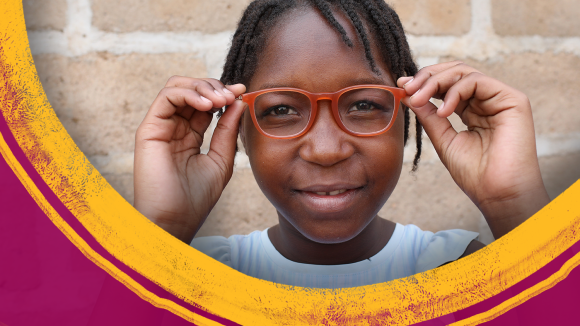 A girl wearing red glasses stands in front of a brick wall.