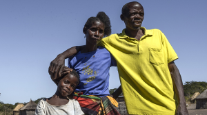 Nalukena stands outside with her mother and father. They are all embracing.