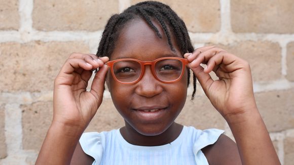 Ivania, a girl from Mozambique, holds her red glasses in front of her eyes.