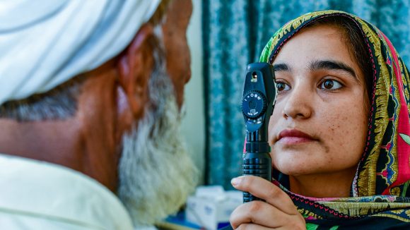 A female optometrist uses an ophthalmoscope to examine a man's eyes.
