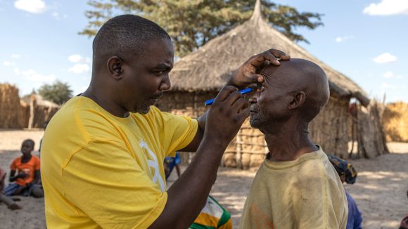 Restman treats a man in a village in Zambia, He is wearing a yellow Sightsavers t-shirt.