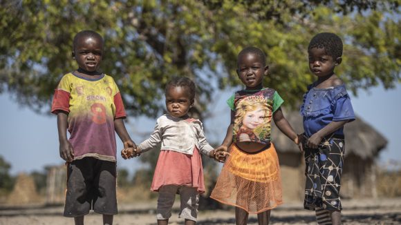 17 month old Sarah (second from left) stands with her three cousins. They are all holding hands.