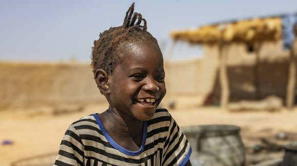 A young girl laughs while standing outside a house.