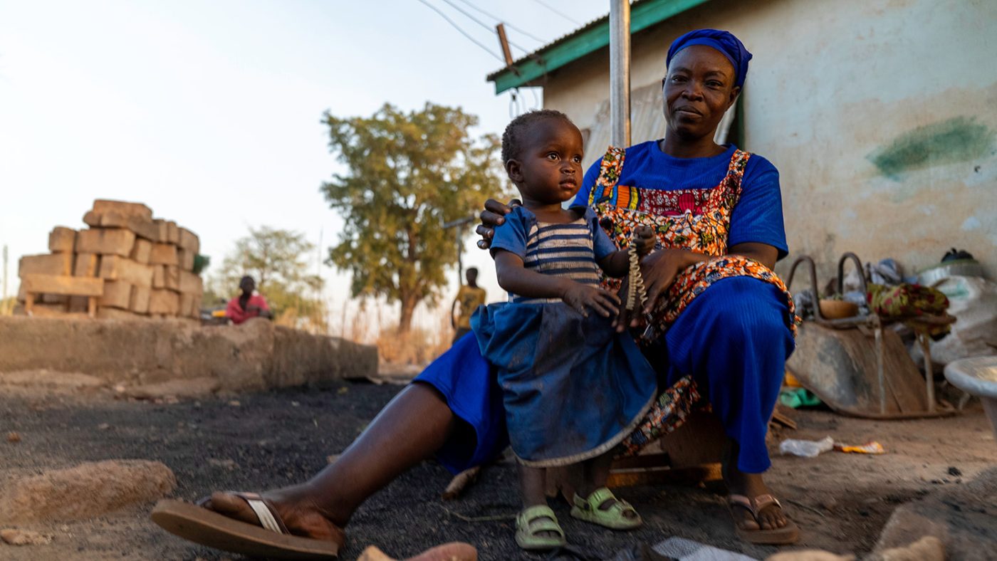 Akambole sits outside with a young girl on her lap.