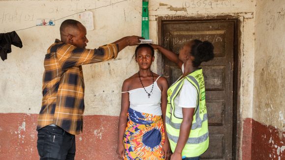 A community member is being measured against a dose pole to determine how much medication for river blindness is needed.